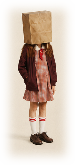 A girl in school uniform stands alone, a paper bag over her head.